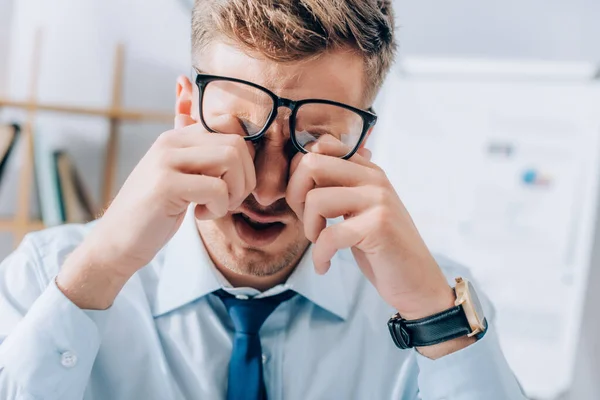 Exhausted businessman rubbing eyes while working in office